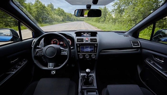 View from the back seat of a driver navigating a modern car on a city road during sunset, showing the dashboard and steering wheel.